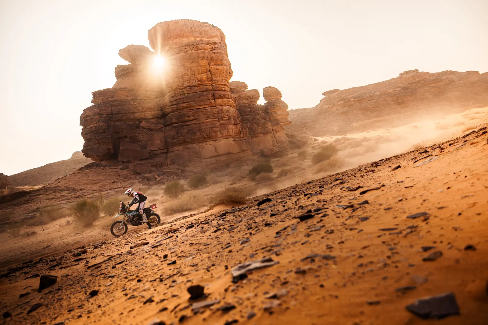 Un pilota passa sotto una formazione di roccia nel deserto, controluce, Dakar 2026